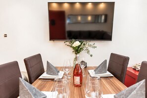 A dining table with four chairs, a vase with flowers, and a bottle of wine. - Smart Resorts - Haus Rubin - Studio-apartment 102 mit Terrasse, Max. 4 Personen - Smart Resorts Haus (Winterberg)