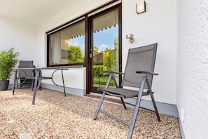 A patio with two chairs and a table, a potted plant, and a view of a garden through a glass door. - Smart Resorts - Haus Rubin - Studio-apartment 102 mit Terrasse, Max. 4 Personen - Smart Resorts Haus (Winterberg)