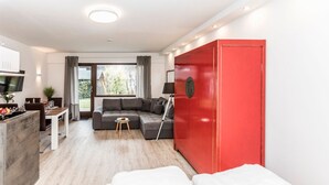 Ein modernes Hotelzimmer mit grauem Sofa, einem roten Kleiderschrank, einem Essbereich mit Tisch und Stühlen sowie einem Fernseher.