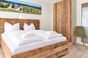 A bedroom with a wooden bed frame, white bedding, and a view of a landscape through a window. - Smart Resorts - Haus Brilliant - Ferienwohnung 603 mit 1 Schlafzimmer und Balkon, Max. 6 Personen - (Winterberg)