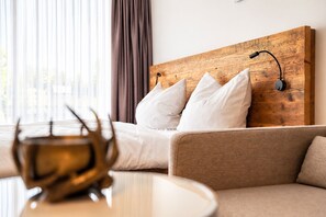 Habitación de hotel con cabecera de madera, ropa de cama blanca, sofá marrón y una mesa con un objeto decorativo.