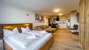 Ein Hotelzimmer mit einem großen Bett, einem Schlafsofa, einem kleinen Tisch und einer Küchenzeile im Hintergrund.