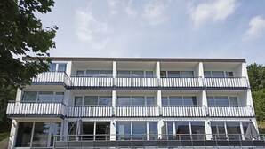 Ein mehrgeschossiges Gebäude mit Balkonen, großen Fenstern und einem Parkplatz davor.