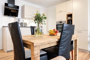 Una cocina moderna con una mesa de madera, sillas negras, un florero con flores y un cuenco de frutas.