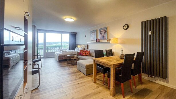 Ein modernes Wohnzimmer mit einem Holzesstisch, schwarzen Stühlen, einer Couch und einem Balkon mit Blick.