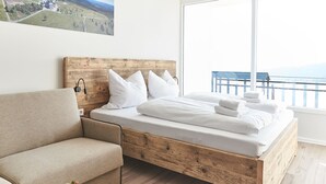Ein Schlafzimmer mit einem Holzkopfteil, einem Bett mit weißen Leinentüchern, einem beigen Sofa und einer Obstschale auf einem Holztisch.