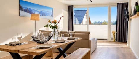 Comedor con mesa de madera, bancos y vista al exterior a través de amplios ventanales.