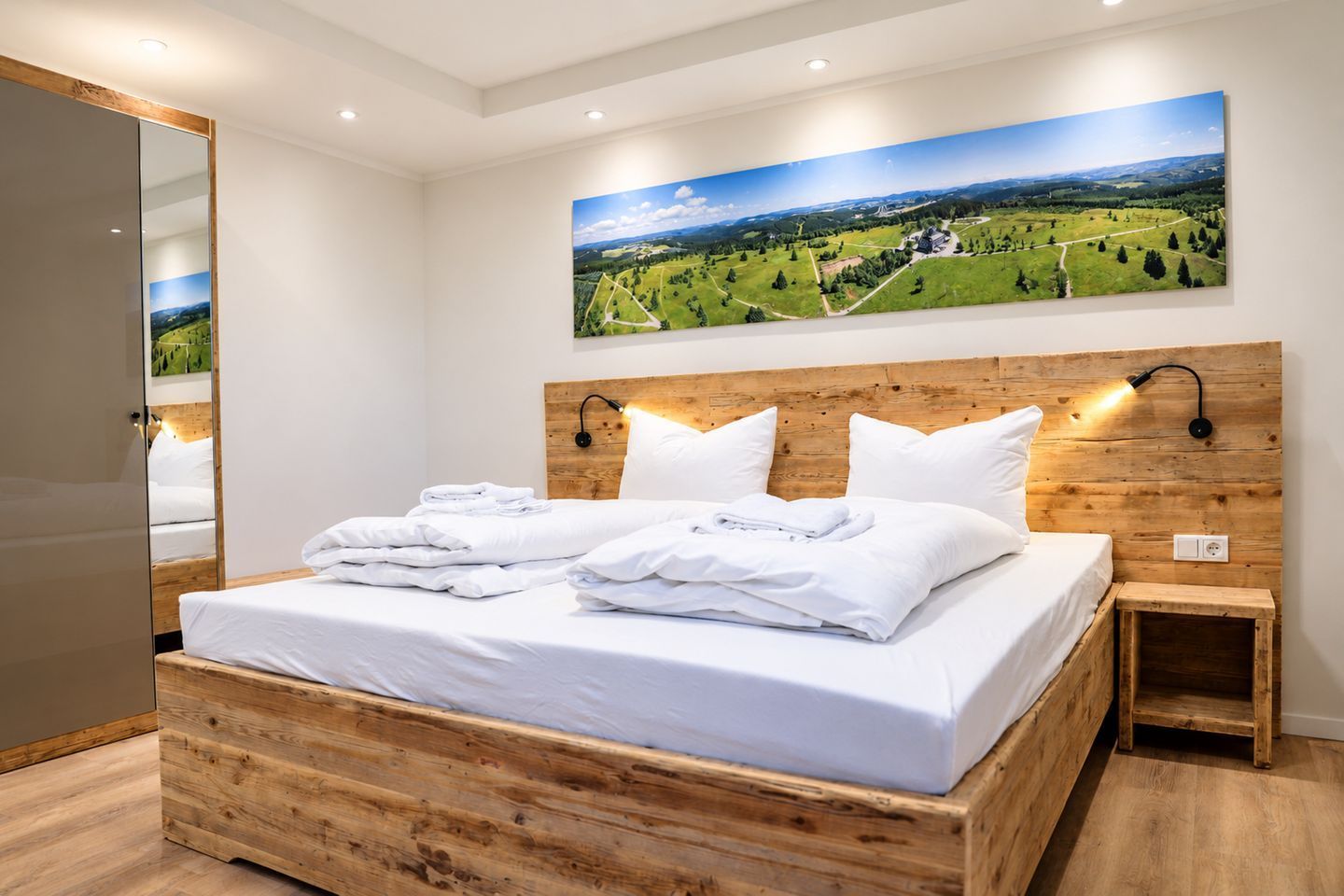 A bedroom with a wooden headboard, a large landscape painting, and a neatly made bed with white linens.