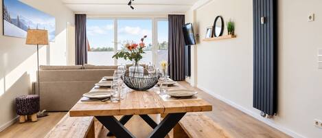 A dining area with a wooden table set for four, a sofa, and a view of the outdoors.