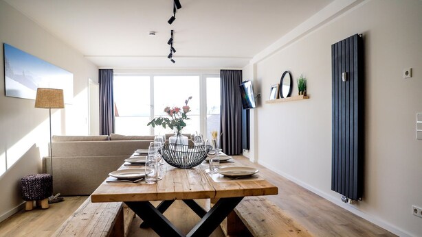 A dining area with a wooden table set for four, a sofa, and a TV mounted on the wall.