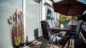An outdoor patio with a table and chairs, a potted plant, and a large umbrella.