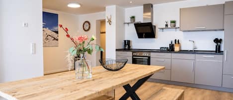 A modern kitchen with a wooden dining table, a vase with flowers, and a black bowl.