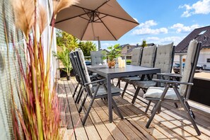 An outdoor patio with a table and chairs, a large umbrella, and a view of houses in the background.