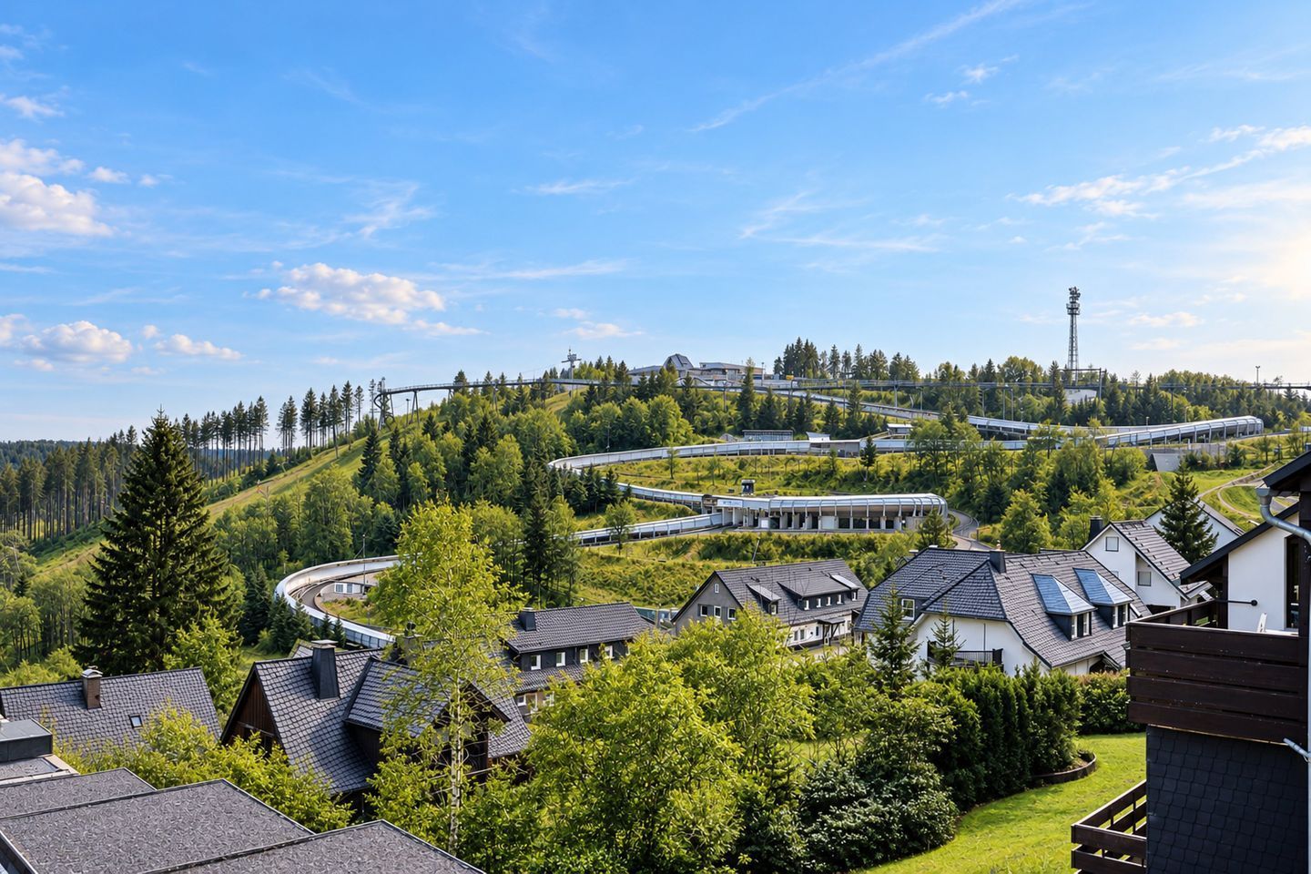 A residential area with houses, a curved train track, and a forested hill.