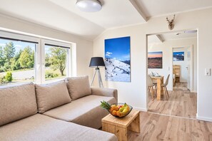 A modern living room with a sofa, a dining area, and a view of a snowy landscape through the window.