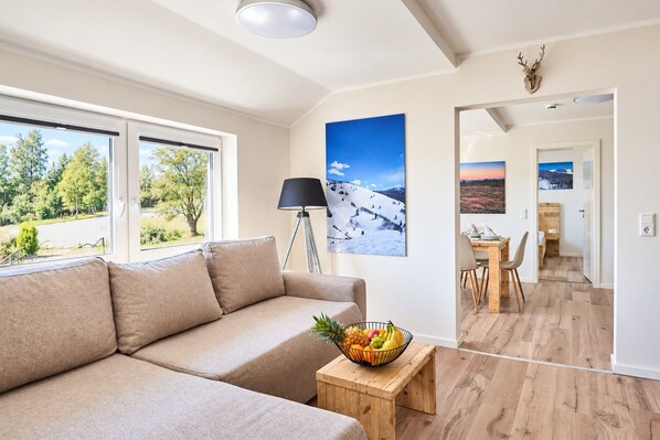 A modern living room with a sofa, a dining area, and a view of a snowy landscape through the window.