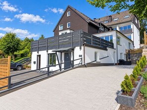 A modern two-story house with a covered outdoor area, a driveway, and a gated entrance.