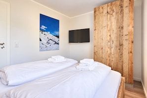 Habitación de hotel con dos camas individuales, un televisor montado, pared de paneles de madera y un cuadro de un paisaje nevado.