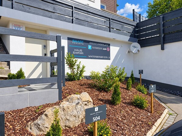 A sign for Smart Resorts with a private parking area, a gate, and a landscaped area with rocks and plants.