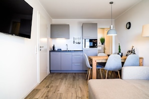 Un espacio habitable compacto con kitchenette, comedor y televisor montado en la pared.