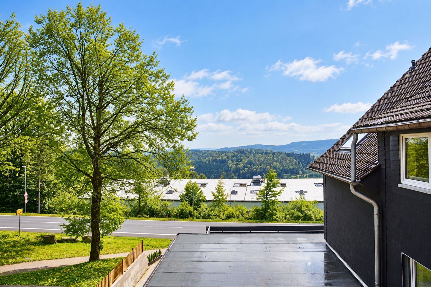 A residential building with a balcony overlooking a road and a forested area.