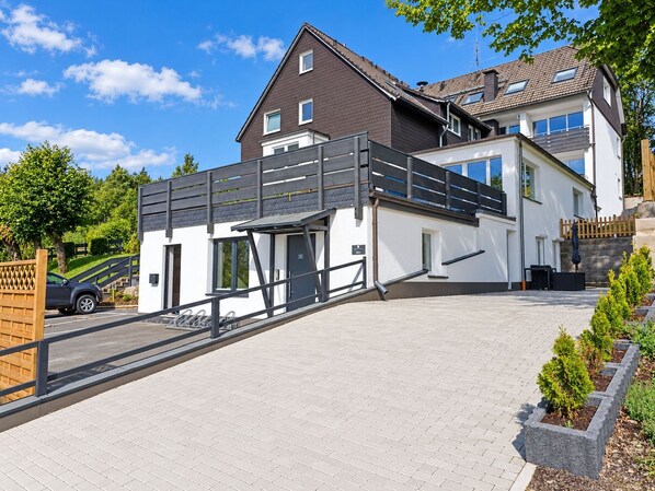 A modern two-story house with a covered outdoor area, a driveway, and a gated entrance.