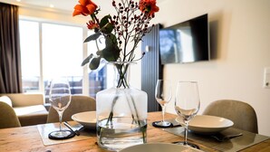 A dining table set with clear glassware, a vase with flowers, and a modern interior with a TV mounted on the wall.