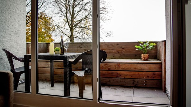 A wooden bench with a potted plant, a table with a candle and a wine bottle, and chairs.