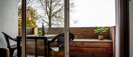 A wooden bench with a potted plant, a table with a candle and a wine bottle, and chairs.