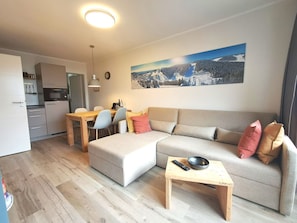 A modern living room with a sofa, a dining table, and a kitchen in the background.