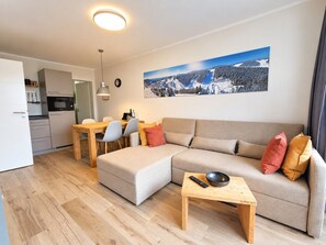 A modern living room with a sofa, a dining table, and a kitchen area.