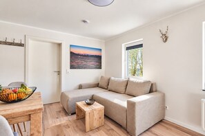 Una sala moderna con un sofá seccional color beige, una mesa de centro de madera y un frutero sobre una mesa de madera.