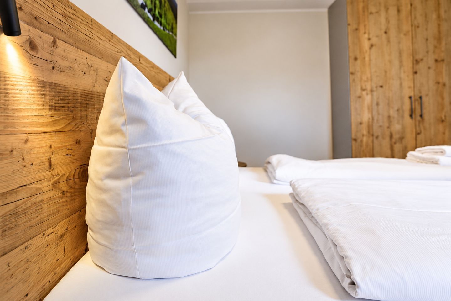 Ein Schlafzimmer mit einem Holz-Kopfteil, einem weißen Kopfkissen und ordentlich zusammenglegter weißer Bettwäsche.