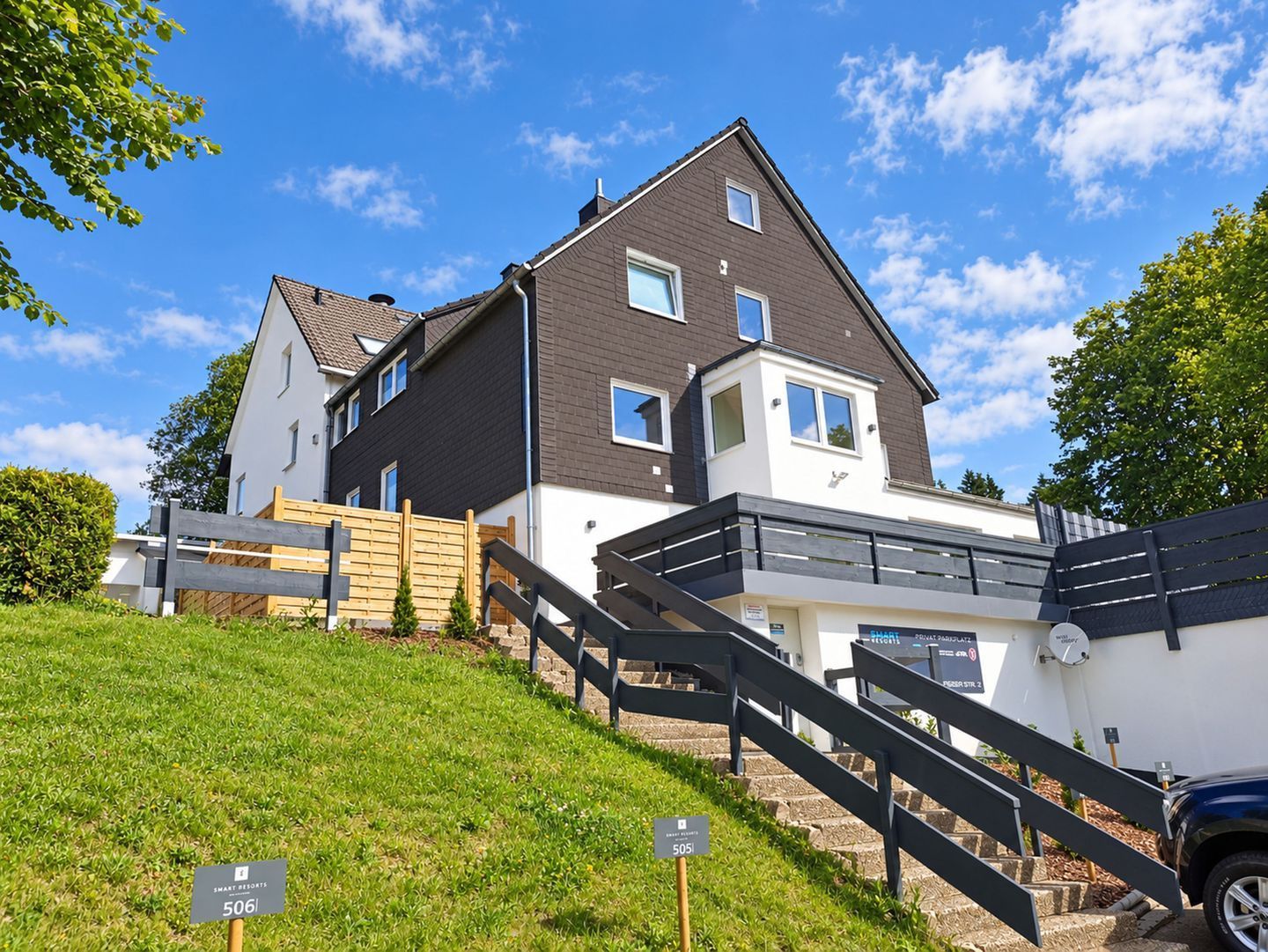 A two-story residential building with a modern design, a visible staircase, and a well-maintained lawn.