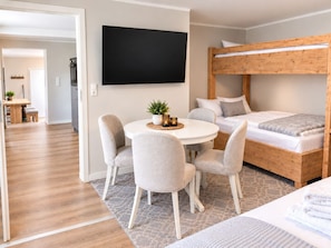 A modern bedroom with a bunk bed, a round dining table with chairs, and a flat-screen TV mounted on the wall. - Smart Resorts- Haus Saphir - Wohnung 501 - Smart Resorts Haus Saphir (Winterberg)