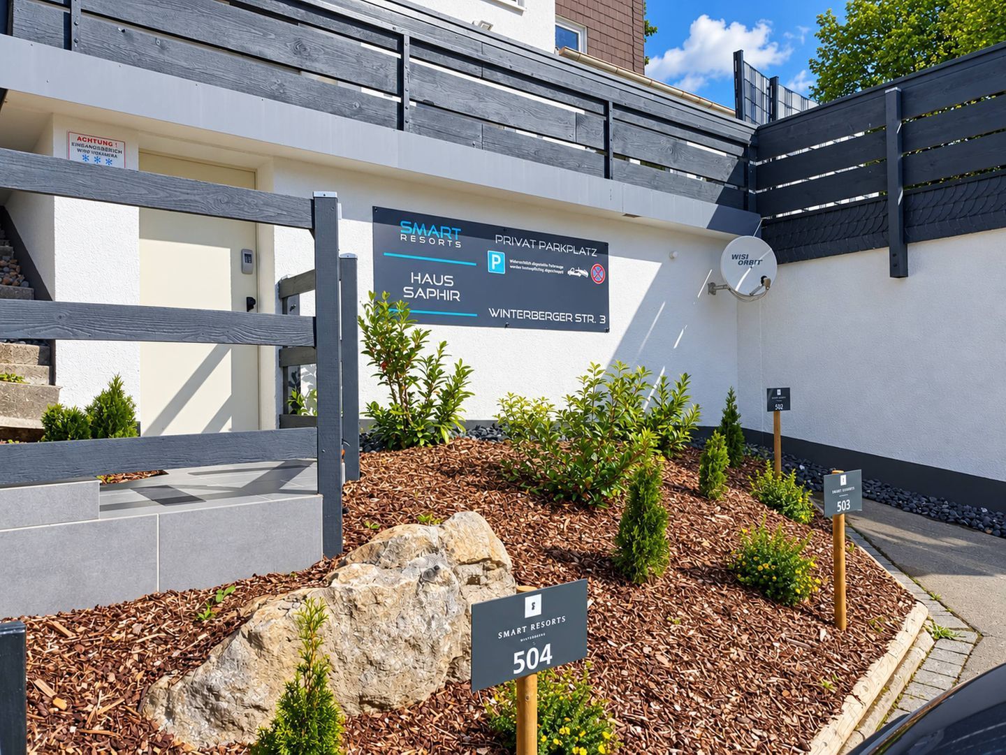 A sign for Smart Resorts with a private parking area, a gate, and a landscaped area with rocks and plants.