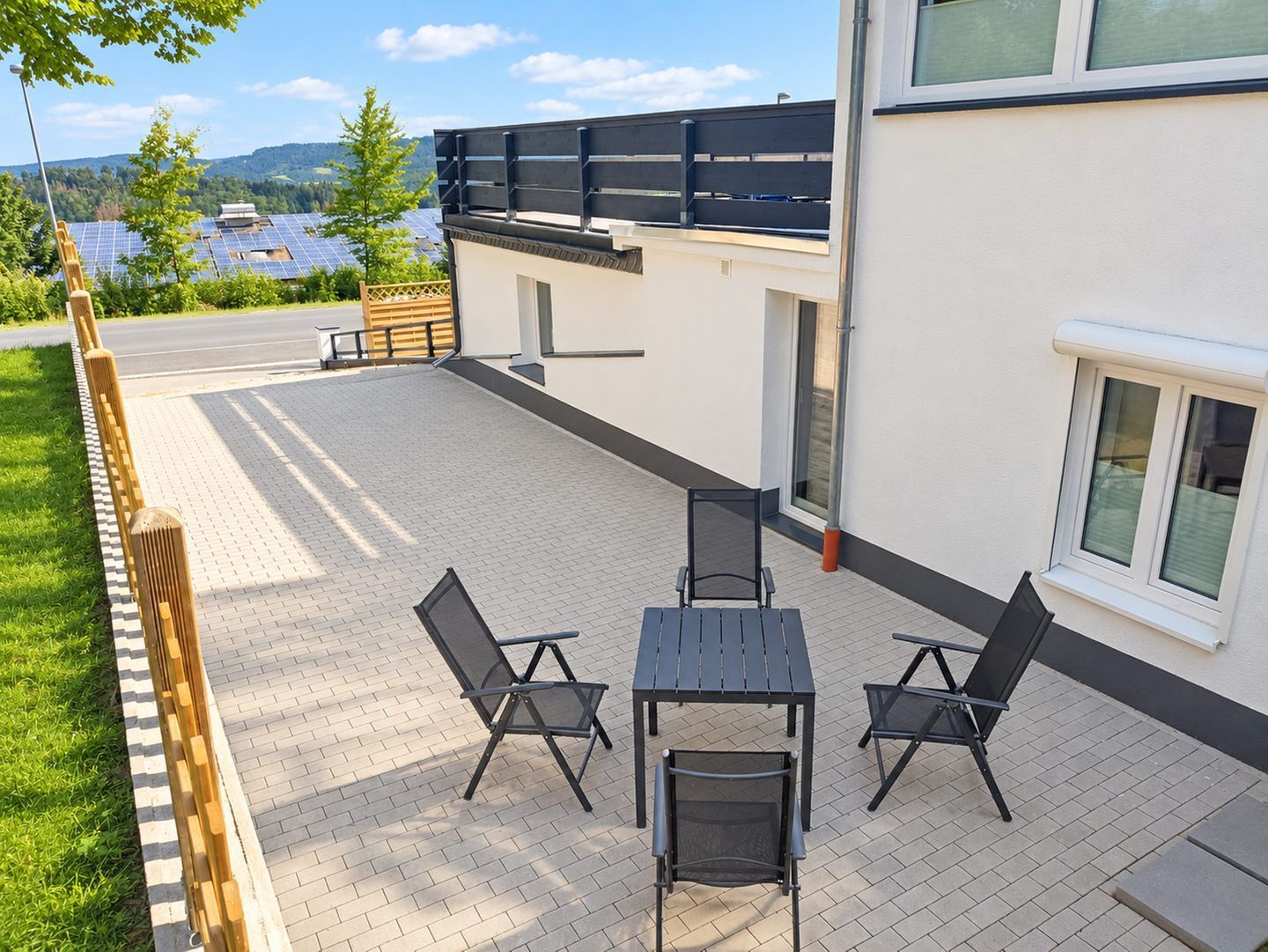 An outdoor patio with a table and chairs, a wooden fence, and a view of solar panels in the background.
