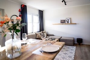 Un coin repas avec une table en bois dressée pour quatre personnes, un canapé et une étagère murale ornée de tableaux encadrés.