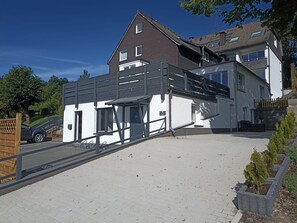 Une maison moderne à deux étages, dotée d’un balcon et d’un espace extérieur couvert.
