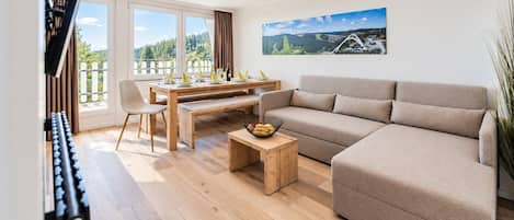 Una sala de estar moderna con un sofá, una mesa de comedor para cuatro personas y un ventanal con vistas a zonas verdes.