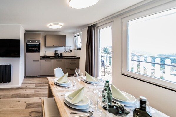 A modern kitchen with a dining area, a TV, and a balcony with a view.