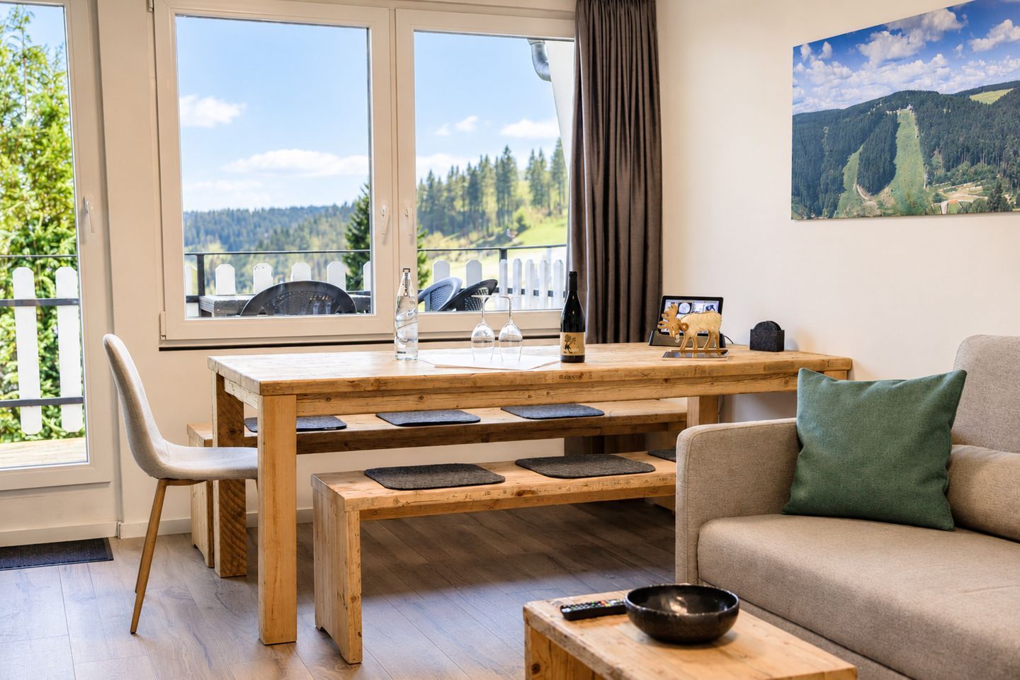 Una sala de estar acogedora con una mesa de comedor de madera, un sofá y vistas a un bosque a través de grandes ventanales.