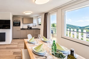 A modern kitchen with a dining area, a view of the countryside, and a table set for two.