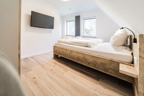 A bedroom with a wooden bed frame, a mounted TV, and a window with blinds.