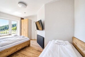 Une chambre avec deux lits, une télévision et une fenêtre donnant sur les arbres.