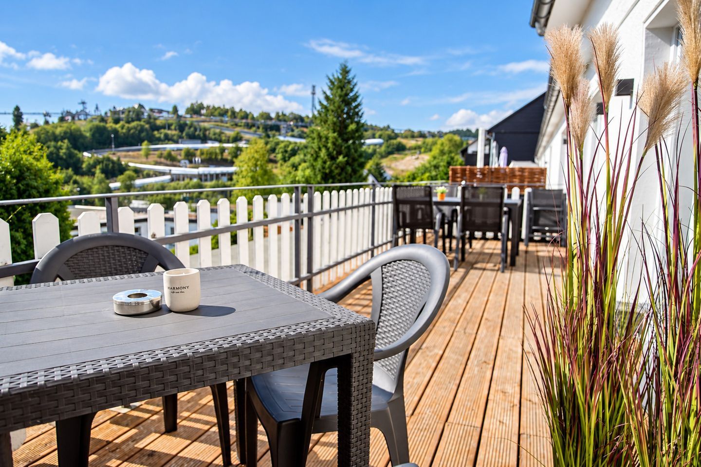 A wooden deck with outdoor furniture, a white fence, and a view of a green landscape.