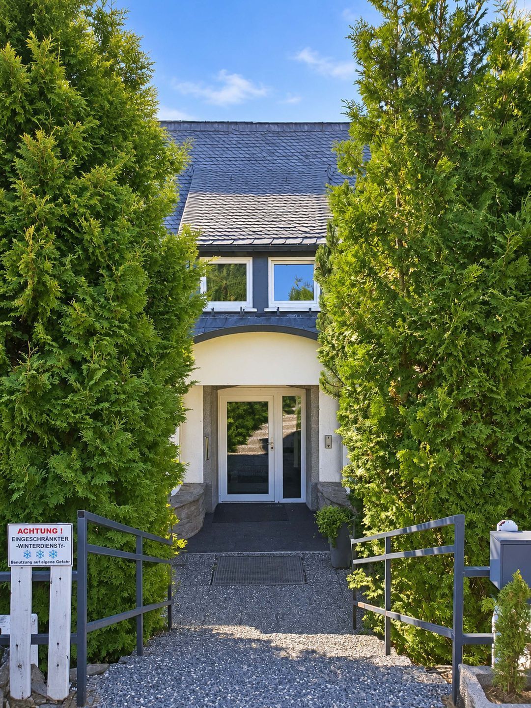 A building with a double door entrance, surrounded by trees, and a sign indicating a winter service area.