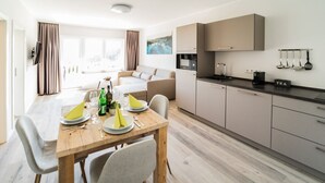 A modern kitchen with a dining area, wooden table, and light-colored cabinets. - Smart Resorts - House Diamant - Apartment 705 with balcony, max. 5 persons - (Winterberg)