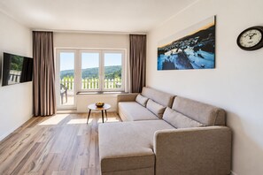 Una sala de estar moderna con un sofá color beige, una mesita redonda y un ventanal con cortinas.