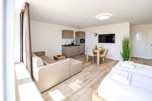 A hotel room with a bed, a sofa, a dining table with chairs, a kitchen area, and a TV mounted on the wall. - Smart Resorts - Haus Diamant - Studio-apartment 708 mit Balkon, Max. 4 Personen - Smart Resorts Haus (Winterberg)